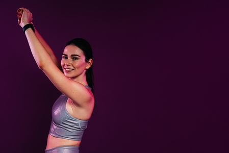 Slim woman raising her hands up while warming up  standing against a magenta background