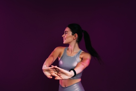 Slim woman in silver fitness wear doing warming up exercises against a magenta background