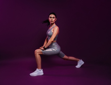 Slim female in silver fitness attire warming up her body against a magenta background