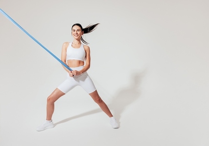Slim woman with resistance band working out over white background