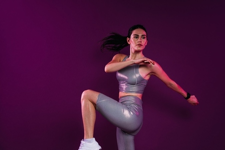 Young slim woman in silver sportrswear warming up her body over magenta backdrop