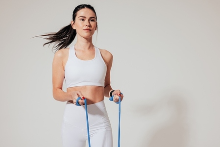 Confident female athlete in white sports clothes exercising with resistance band