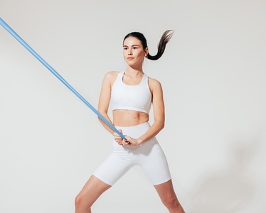 Healthy slim woman in white sports clothes practicing with resistance band in studio