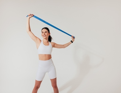 Healthy smiling woman in white fitness wear warming up with a resistance band