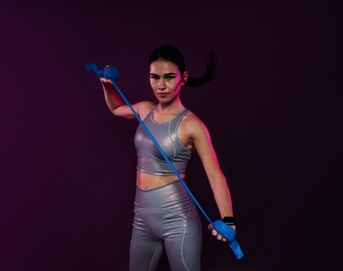 Muscular female in sportswear practicing with a resistance band against a magenta background in studio