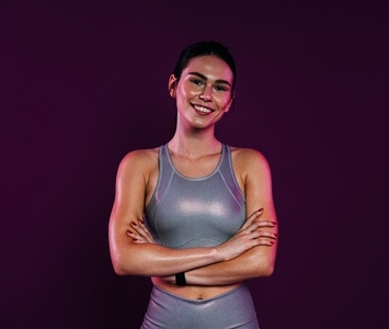 Smiling sportswoman with crossed arms wearing silver sportswear looking at the camera against a magenta background