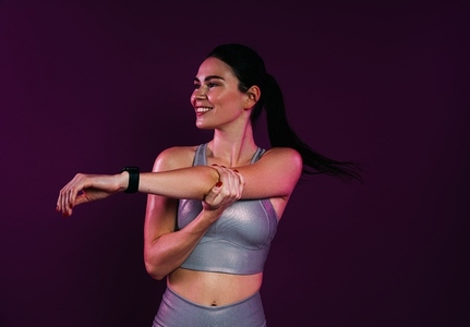 Smiling slim female flexing her hand against a magenta background in studio