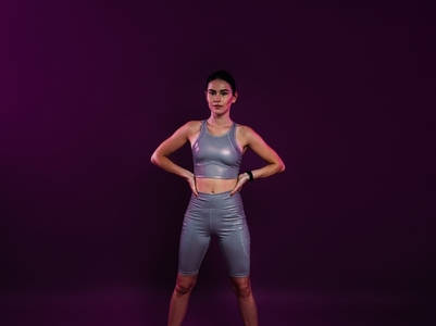 Young confident sportswoman in silver fitness attire with hands on hips