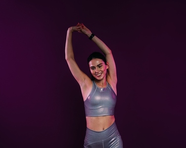 Positive woman in silver sportswear flexing her hands on a magenta background