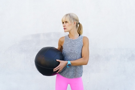 Adult woman in sportswear standing with medicine ball in daylight
