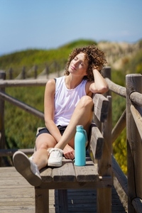 Happy young woman resting on wooden bench in sunlight