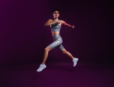 Full length of slim woman in silver sports clothes running and jumping over a magenta backdrop