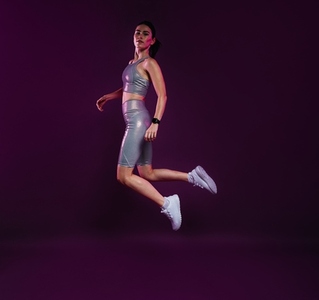 Full length of a healthy woman in silver sportswear jumping in the air over magenta backdrop