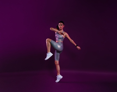 Full length of slim healthy woman warming up over a magenta background  wearing silver fitness attire