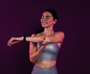 Young smiling female with closed eyes stretching and flexing her hands over magenta background in studio
