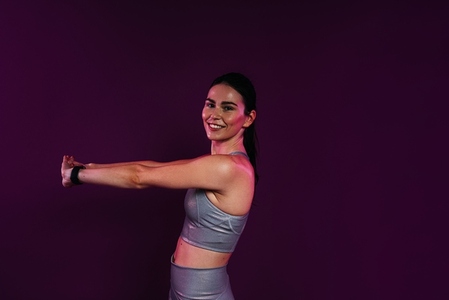 Side view of young smiling female stretching and flexing her hands over magenta background in studio