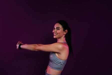 Young smiling woman stretching and flexing her hands over magenta background in studio