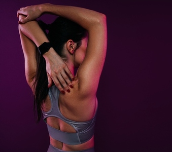 Rear view of young muscular female stretching her hand against a magenta background