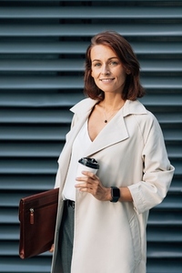Middle aged businesswoman holding a coffee to go cup and leather folder while standing outdoors