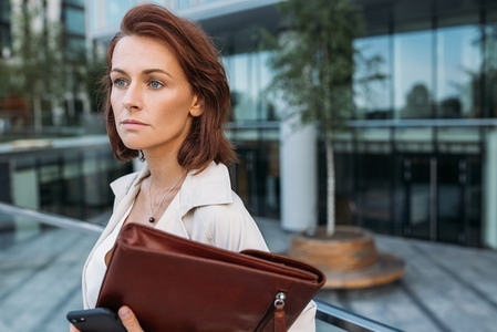 Close up portrait of a middle aged businesswoman holding a leather folder against a business building