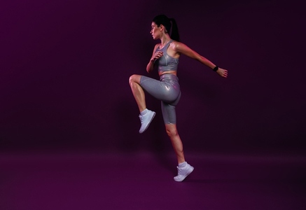 Full length of a young slim jogger practicing over a magenta backdrop  Female in silver fitness attire jumping