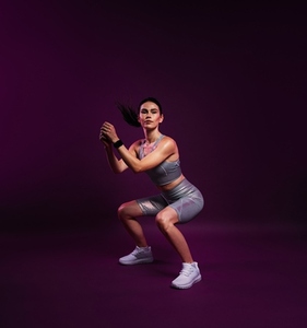 Full length of a slim female in silver sportswear doing sit ups over a magenta background