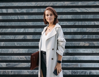 Stylish middle aged female entrepreneur holding leather folder standing outdoors