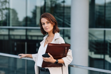 Confident business woman with ginger hair looking at camera  Middle aged female with folder at business building
