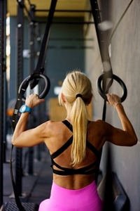 Unrecognizable fit lady exercising with gymnastic rings in fitness center