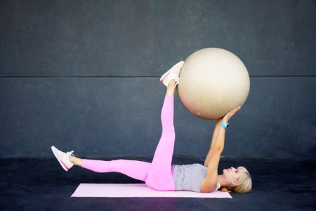 Flexible young woman doing yoga with fit ball in gym while lying on mat