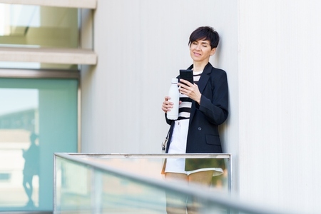 Businesswoman using smartphone and holding bottle of water