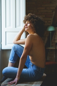 Topless female in jeans sitting near window