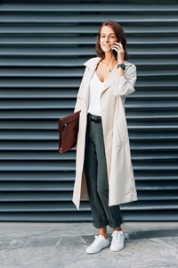 Full length of a stylish businesswoman with a folder talking on a mobile phone outdoors