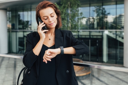 Middle aged businesswoman looking at her smartwatch while talking on mobile phone