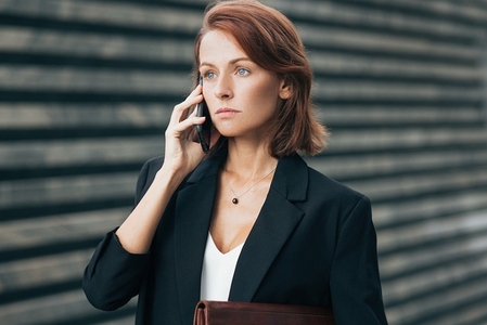 Confident and serious businesswoman with ginger hair talking on mobile phone