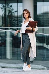 Confident middle aged female holding a leather folder looking at camera standing at an office building