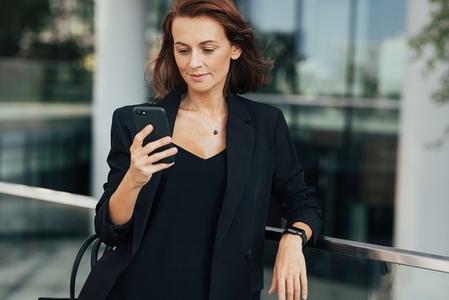 Confident middle aged businesswoman standing outdoors and looking at a smartphone