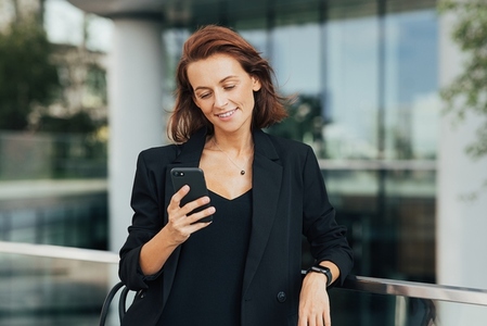 Smiling woman with ginger hair wearing formal wear looking at her smartphone