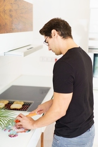 Adult man standing near cooking range and cutting tomato in kitchen