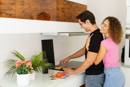 Happy adult man standing near cooking range and smiling woman embracing from behind