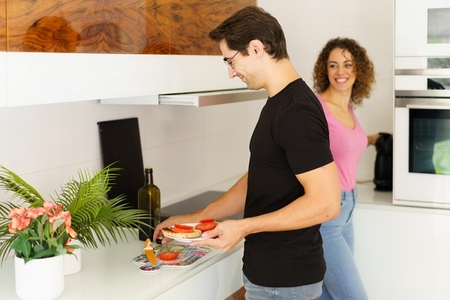 Happy adult man standing near cooking range with woman and arranging salad in kitchen