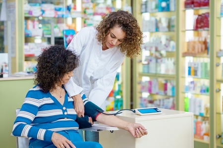 Young woman pharmacist checking blood pressure of lady customer in pharmacy