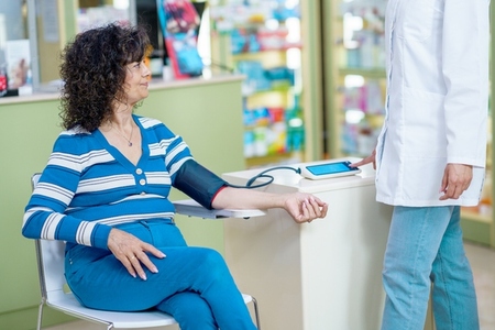 Unrecognizable woman pharmacist checking blood pressure of lady customer in pharmacy