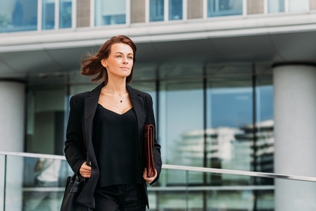 Confident middle aged businesswoman holding a leather folder walking against an office building