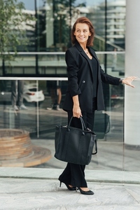 Full length of a confident middle aged businesswoman in formal wear with a bag standing against an office building