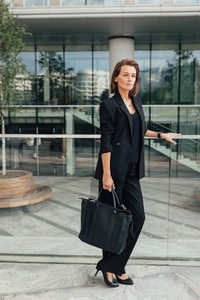 Full length of a middle aged female in black formal wear leaning a railing standing against office building