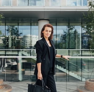 Portrait of a confident middle aged female in formal wear with a bag against an office building