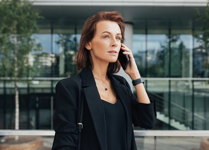 Side view of a beautiful businesswoman talking on a mobile phone against glass building