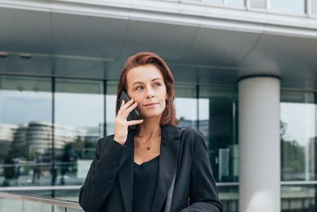 Portrait of a middle aged female in formal wear talking on a mobile phone against an office building