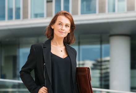 Smiling middle aged businesswoman walking against office building  Portrait of a middle aged female in formal wear